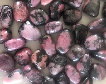 May include: A collection of polished rhodonite stones. The stones are a mix of pink and black, with varying patterns and sizes. The smooth, rounded stones are arranged closely together, creating a visually appealing display. The pink hues range from light to deep shades.