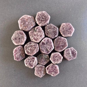 K&ouml;nnte beinhalten: Eine Sammlung von 14 rosafarbenen Rubingesteinen, jeder mit einer sechseckigen Form und einer rauen, nat&uuml;rlichen Oberfl&auml;che.