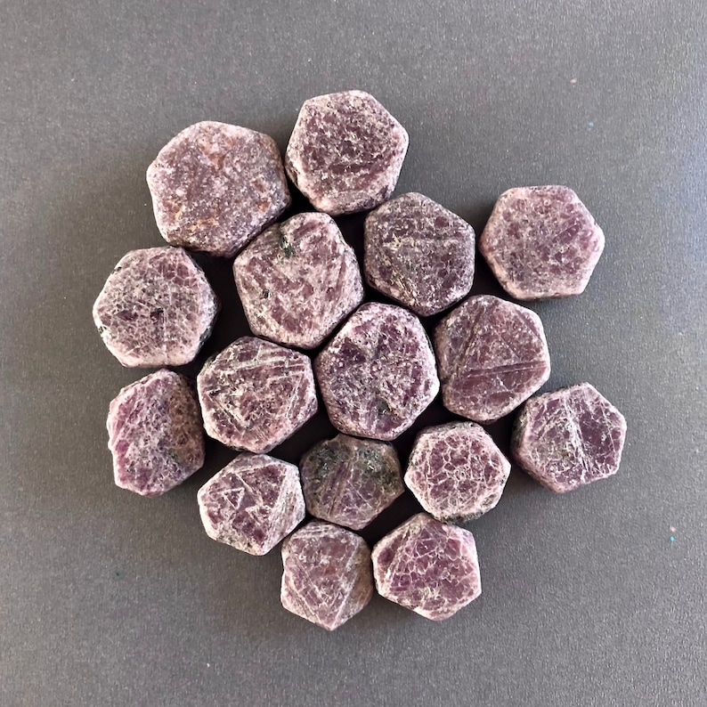 K&ouml;nnte beinhalten: Eine Sammlung von 14 rosafarbenen Rubingesteinen, jeder mit einer sechseckigen Form und einer rauen, nat&uuml;rlichen Oberfl&auml;che.