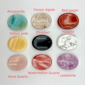 May include: Nine oval-shaped polished stones, each with a different color and pattern. The stones are arranged in three rows of three. The stones are labeled with their names: Amazonite, Flower Agate, Red Jasper, Yellow Jade, Obsidian, Howlite, Rose Quartz, Watermelon Quartz, and Lepidolite.