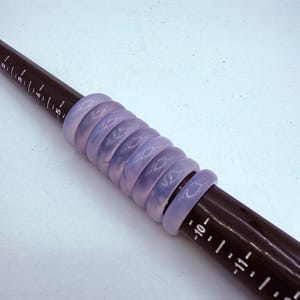 May include: A stack of eight purple silicone rings with a diamond pattern on a black ruler.