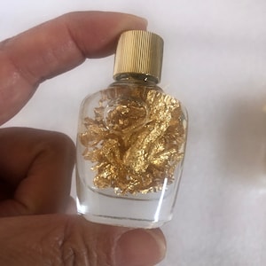 May include: A small, clear glass bottle with a gold cap. The bottle is filled with gold flakes.