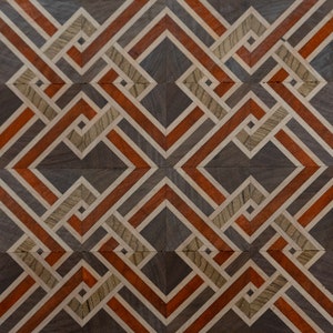 May include: A geometric pattern of wood inlay with alternating squares of light brown, dark brown, and orange wood. The pattern is symmetrical and creates a visually interesting design.