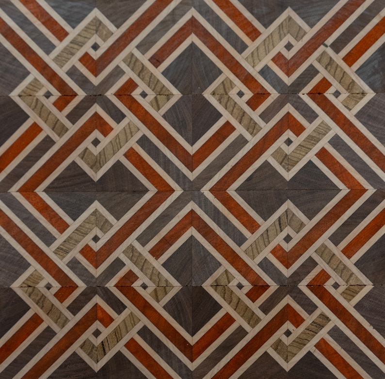 May include: A geometric pattern of wood inlay with alternating squares of light brown, dark brown, and orange wood. The pattern is symmetrical and creates a visually interesting design.