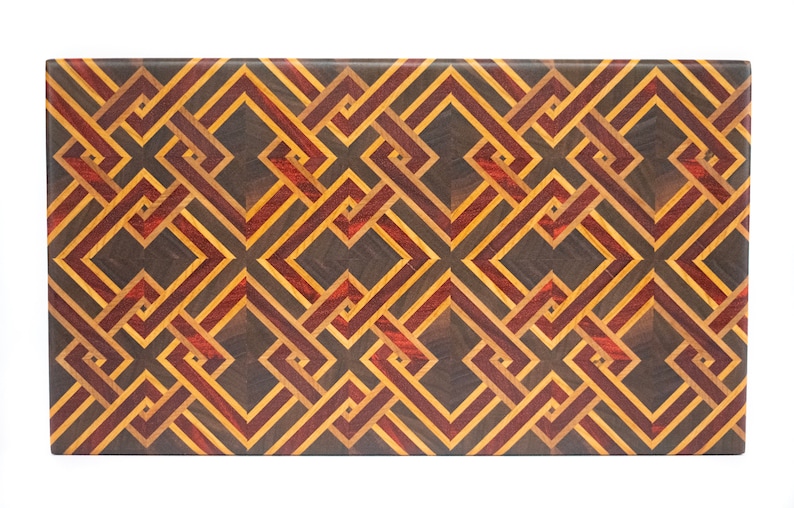 May include: A rectangular wooden cutting board with a geometric pattern made of different colored woods. The pattern is made of squares and rectangles, and the colors are brown, red, and yellow.