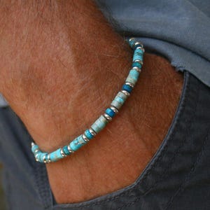 Peut inclure: Un bracelet de perles turquoise et argent. Le bracelet est porté au poignet, le bras reposant dans une poche. Les perles sont un mélange de turquoise et d'argent, créant une ambiance décontractée. Un accessoire élégant.