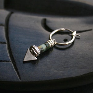 Könnte beinhalten: Silberner Creolenohrring mit einem grünen und silbernen Pfeil-Anhänger.