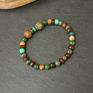 May include: A green, brown, and gold beaded bracelet with a decorative metal bead.