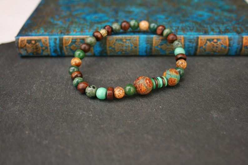 May include: A beaded bracelet with brown, green, and beige beads. The bracelet has a larger, patterned bead in the center.