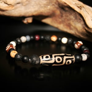 May include: A black beaded bracelet with a brown and white patterned stone charm. The bracelet also features black lava beads and other natural stone beads.