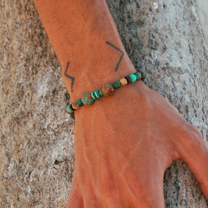 May include: A beaded bracelet with green and brown stones. The bracelet is on a person's wrist.