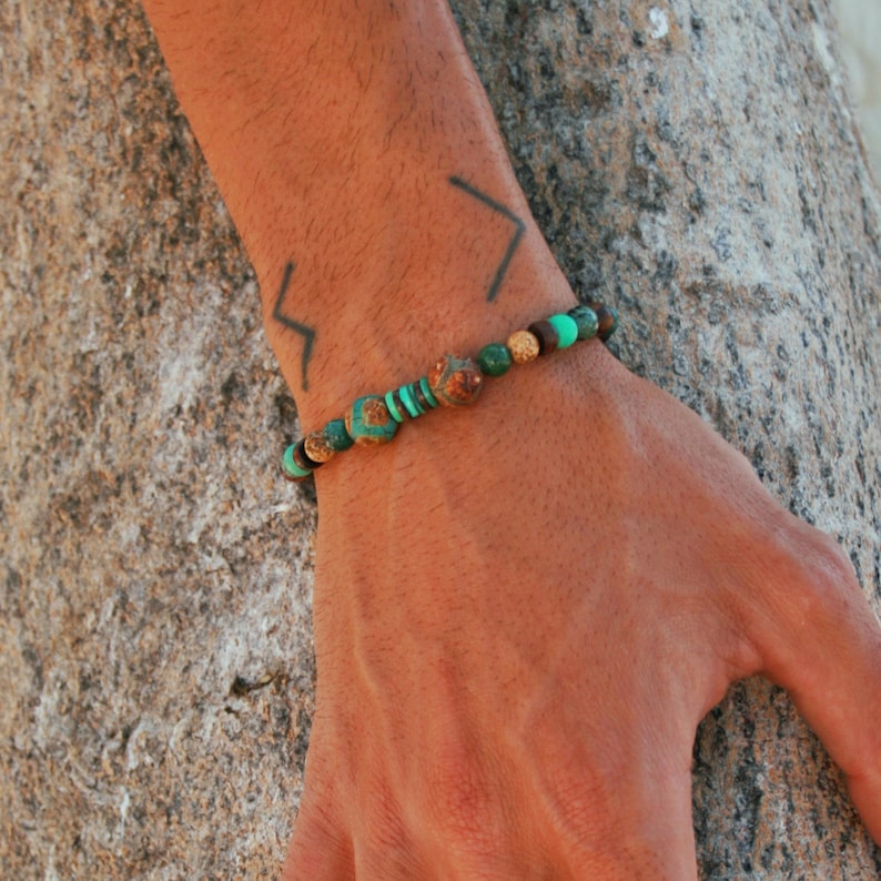 May include: A beaded bracelet with green and brown stones. The bracelet is on a person's wrist.