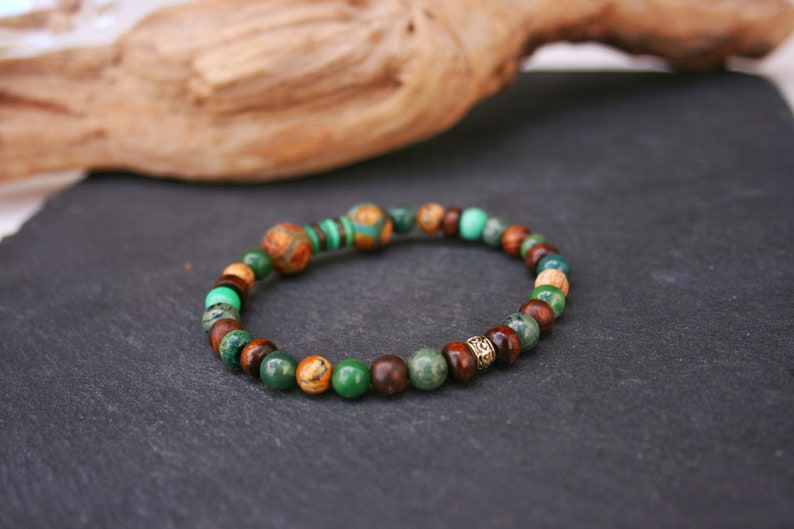 May include: A green, brown, and gold beaded bracelet with a decorative metal bead.