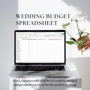 May include: A laptop computer displaying a wedding budget spreadsheet on the screen. The spreadsheet has columns for item, total cost, amount already paid, and total owing. The laptop is on a white surface with a white flower in the background.