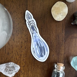 May include: An assortment of spiritual items on a dark wood surface. Includes a lit candle, crystals, a seashell, a sticker of a potion bottle, small glass bottles, a palo santo stick, and a feather.