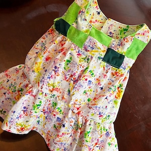 May include: A white sleeveless dress with a colorful paint splatter pattern. The dress has a green and dark green yoke with a square pattern.