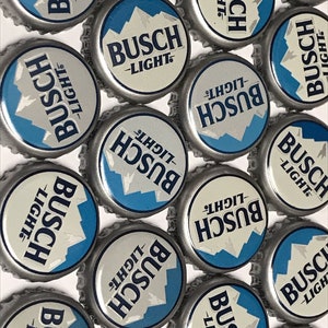May include: A collection of silver bottle caps with a blue and white design. The caps feature the text "Busch Light" in a white font.