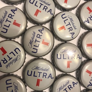 May include: A collection of silver bottle caps with the text "Michelob ULTRA" printed in blue and red. The caps are arranged in a random pattern.