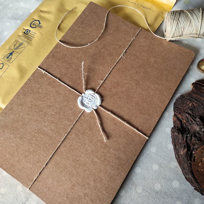 May include: A brown paper package tied with twine and sealed with a white wax seal. The package is sitting on a white fabric surface.