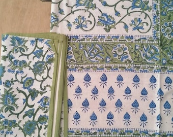 May include: A set of green and blue floral patterned table linens. The tablecloth has a border with a repeating pattern of green and blue leaves. The napkins have a similar floral pattern.