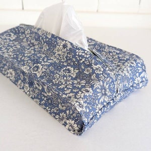 May include: A blue and white floral tissue box cover. The cover is made of fabric and has a white floral pattern on a blue background.