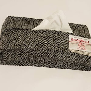 May include: A black and white tweed tissue box cover with a red "Harris Tweed" label. The label says "Hand Woven Cloth" and "Outer Hebrides of Scotland".