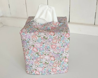 May include: A floral tissue box cover with a white tissue inside. The cover is made of a white fabric with a pink, blue, and green floral pattern.