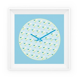 Può includere: Un orologio da parete incorniciato in bianco con uno sfondo blu chiaro e un quadrante circolare con un motivo a limone. Le lancette dell'orologio sono blu.