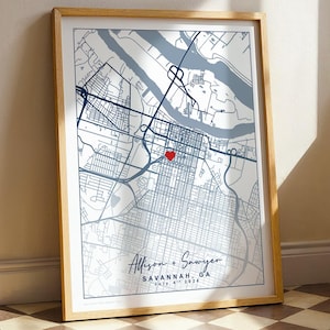 May include: A framed map print of Savannah, GA, featuring a light gray background with dark blue street lines and a river. A small red heart marks a specific location. The text reads Allison + Sawyer, SAVANNAH, GA, and July 6th 2024.