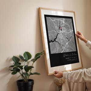 May include: Framed map art print with a black and white city map design. The print includes a red heart-shaped marker and text that reads "Where it all began". The frame is a light wood color.