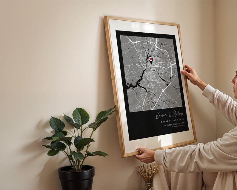 May include: Framed map art print with a black and white city map design. The print includes a red heart-shaped marker and text that reads "Where it all began". The frame is a light wood color.