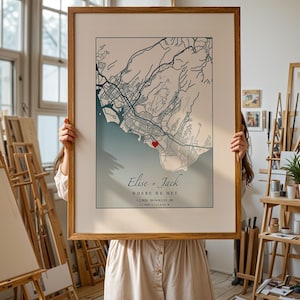 May include: A framed map print featuring a detailed city map with a heart marking a specific location. The map is in shades of blue and beige, with the names "Elise + Jack" and the phrase "WHERE WE MET" displayed below the map.