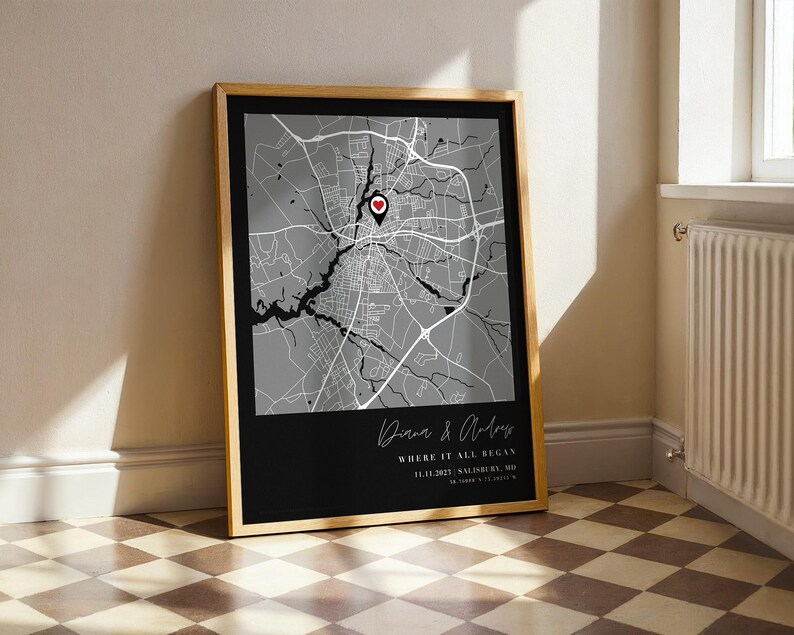 May include: Framed map print with a black and white city map design. The map features a red heart marker and the text "Where it all began" with a date and location. The frame is a light wood color.