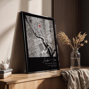May include: Framed black and white map print with a red heart marking a location. The print includes the names "Jordan + Sam" and the text "THE START OF FOREVER" with a date and location. The print is displayed on a wooden surface.