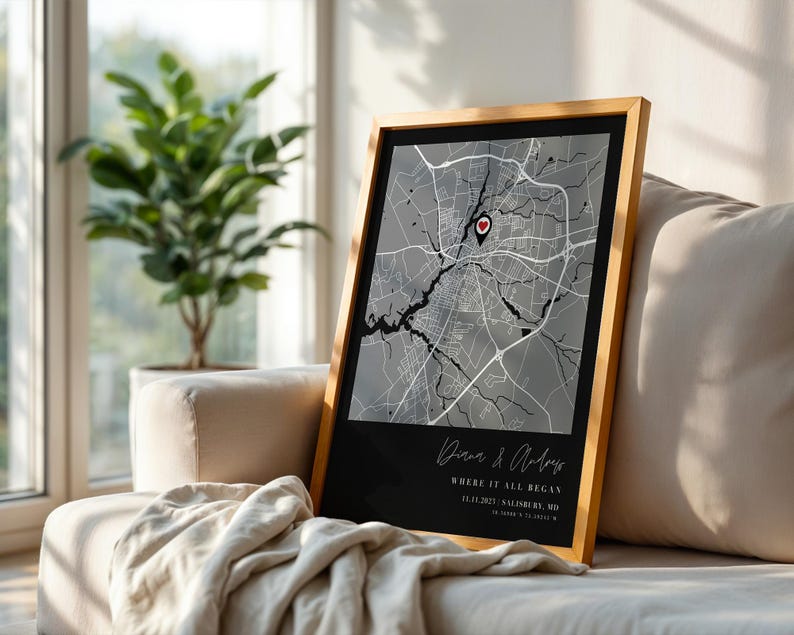 May include: Framed map print with a black and gray city map design. The map is framed in a light wood frame and features a red heart-shaped marker. The text "Diana & Andrew" and "Where it all began" is visible.