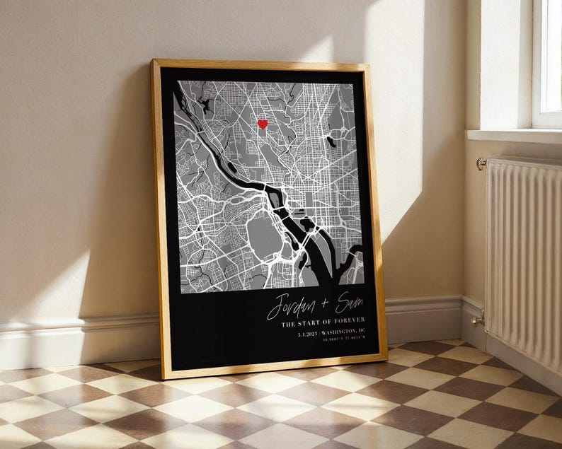 May include: Framed map art print featuring a grayscale city map with a red heart marker. The bottom section is black with white text that reads "Jordan + Sam" and "The Start of Forever". The frame is a light wood color.