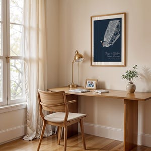 May include: A framed map print with a navy blue background hangs on a beige wall. The map is white with red accents. The text "Taylor & Stephen" is below the map. A wooden desk with a gold lamp, a small photo frame, and a vase with greenery sits below the print.