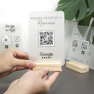 May include: Three acrylic signs with wooden stands. The first sign says "Scan to Pay" with two QR codes. The second sign says "Please leave us a review" with a Google review QR code and the text "Google" with five stars. The third sign says "Thank you" with two QR codes.