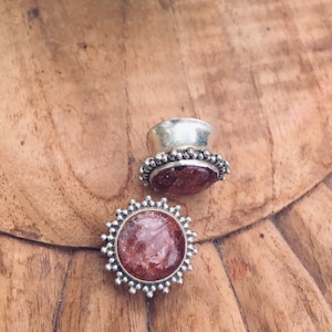May include: Two silver-toned ear plugs with a reddish-brown, speckled stone center. The plugs have a decorative border of small silver beads. One plug is lying flat, and the other is upright, showing the back.