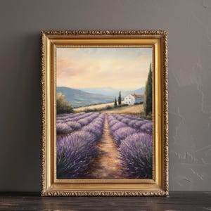 May include: A framed oil painting depicting a landscape with a white farmhouse in the distance, surrounded by rows of purple lavender flowers. The painting has a golden frame and is set against a gray background.