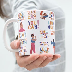 Peut inclure: Une tasse en c&eacute;ramique blanche avec du texte et des illustrations motivants color&eacute;s. Le texte comprend des phrases comme "Saisissez le jour", "Vous pouvez", "Lentement et s&ucirc;rement", "Faites ce que vous aimez", et "Continuez".