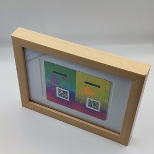 May include: Two colourful gift cards with a rainbow design and a QR code. The cards are framed in a light wood frame.