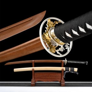 Op de afbeelding: Een Japanse katana-zwaard met een houten schede en handvat, tentoongesteld op een houten standaard. Het lemmet is bruin, het handvat is omwikkeld met zwarte stof en de beschermkap heeft gouden en zilveren accenten. De standaard heeft Japanse karakters.