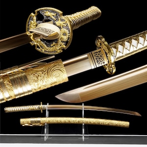 Può includere: Una spada katana dorata con intricati disegni di draghi e fiori. La lama è esposta con il suo fodero, mostrando una lavorazione artigianale dettagliata. L'elsa e la guardia presentano motivi ornati, evidenziando gli elementi decorativi della spada.