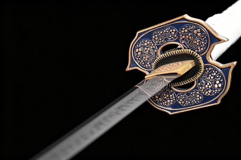 Puede incluir: Primer plano de una katana japonesa. La guarda decorativa azul y dorada presenta un intrincado patr&oacute;n floral. La hoja es plateada con detalles grabados y el mango est&aacute; envuelto en tela blanca. El fondo es negro.
