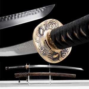 May include: An assortment of Japanese katana swords. The blades have a curved design with intricate patterns. The handles are wrapped in black fabric, and the guards feature detailed carvings. One sword is displayed in its wooden scabbard.