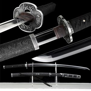 May include: A detailed image of a katana sword with a silver floral guard and a black handle. The blade is shiny and sharp. The scabbard is black with a dragon pattern. The sword is displayed on a clear stand.