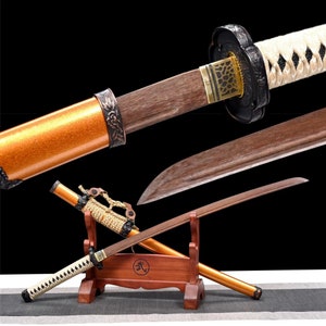 May include: A wooden katana sword with a gold-colored scabbard and a black and white braided handle. The sword is displayed on a wooden stand with the kanji character for "death" on it.