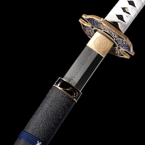 Puede incluir: Primer plano de una katana japonesa. La hoja es plateada y el mango est&aacute; envuelto en material negro texturizado con detalles azules. La guarda es dorada y azul, con dise&ntilde;os intrincados. Se ve el envoltorio blanco del mango de la espada.