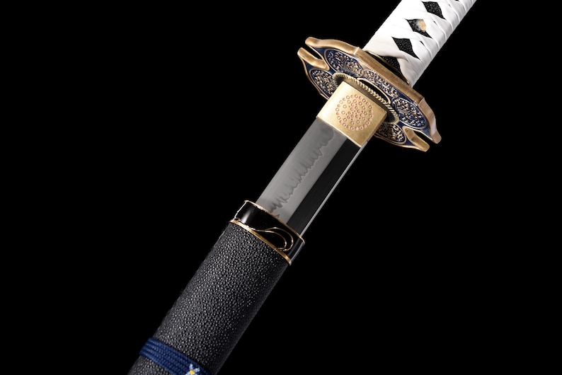 Puede incluir: Primer plano de una katana japonesa. La hoja es plateada y el mango est&aacute; envuelto en material negro texturizado con detalles azules. La guarda es dorada y azul, con dise&ntilde;os intrincados. Se ve el envoltorio blanco del mango de la espada.